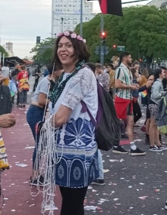 Marlene Wayar smiling at the 2021 Pride march in Buenos Aires, with a crown of pink flowers in her hair and a blue patterned dress.