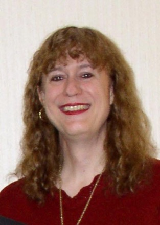 Mary Ann Horton smiling, with long curly auburn hair, in a dark red top.