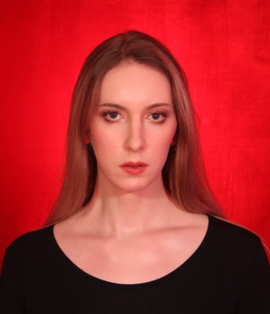 Natalie Wynn against a red backdrop, with long auburn hair, in a black top.